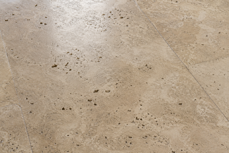Close-up of a pitted travertine floor showing natural pores, holes, and surface voids characteristic of porous travertine stone.